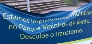 Faixa escrito "estamos implantando melhoria no parque moinhos de vento. desculpe o transtorno"